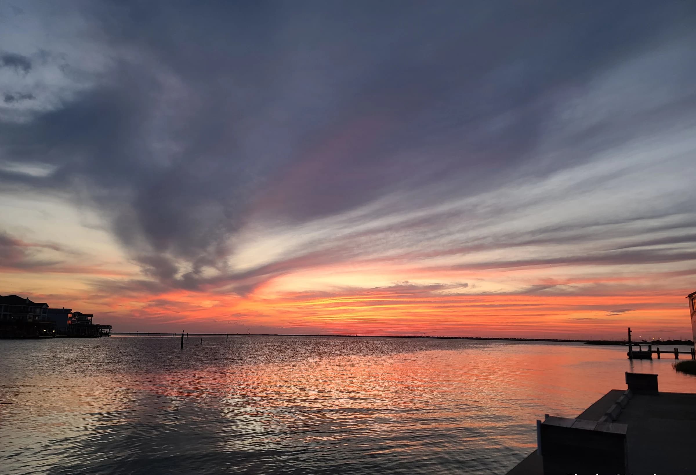 Layered pink and blue clouds stretch over calm water at sunset.