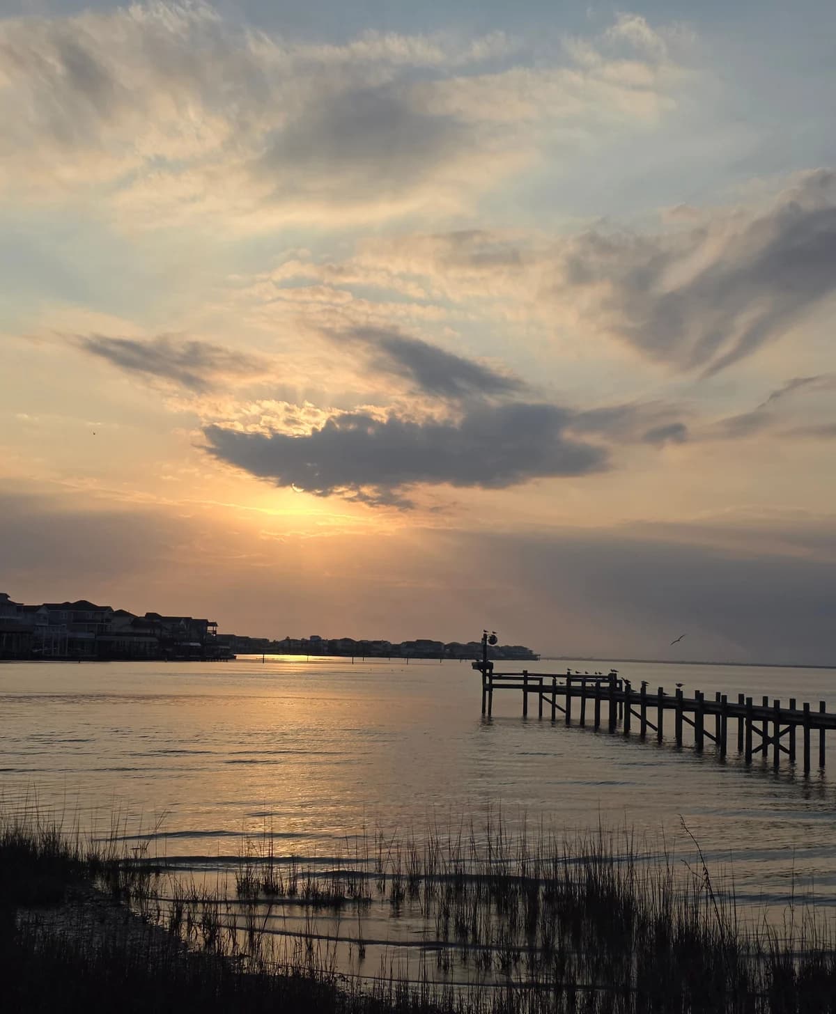 A fishing pier reaches into reflective water beneath softly lit coastal clouds.