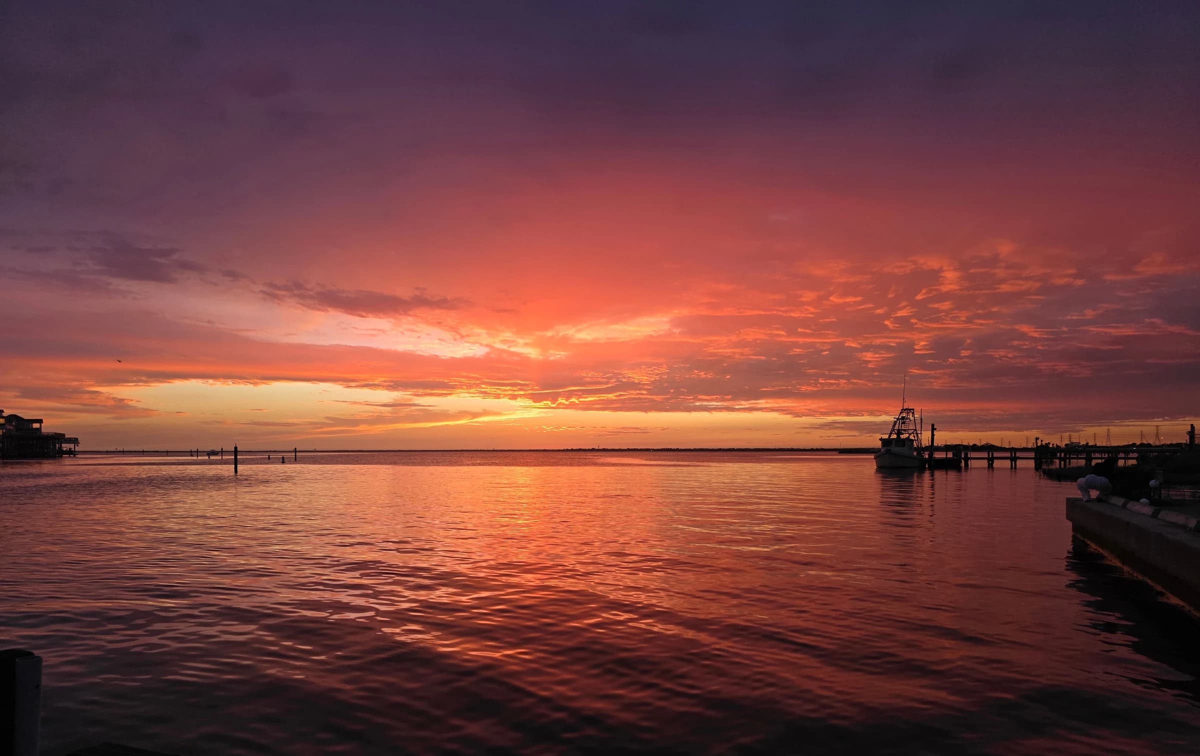 A dramatic red and violet sunset reflects across open water near a small pier.