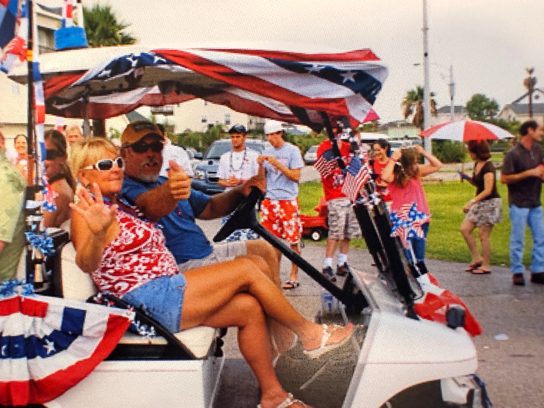 Tom and Kat Fisher sit together in a golf cart decorated with American and Texas flags at an outdoor gathering.