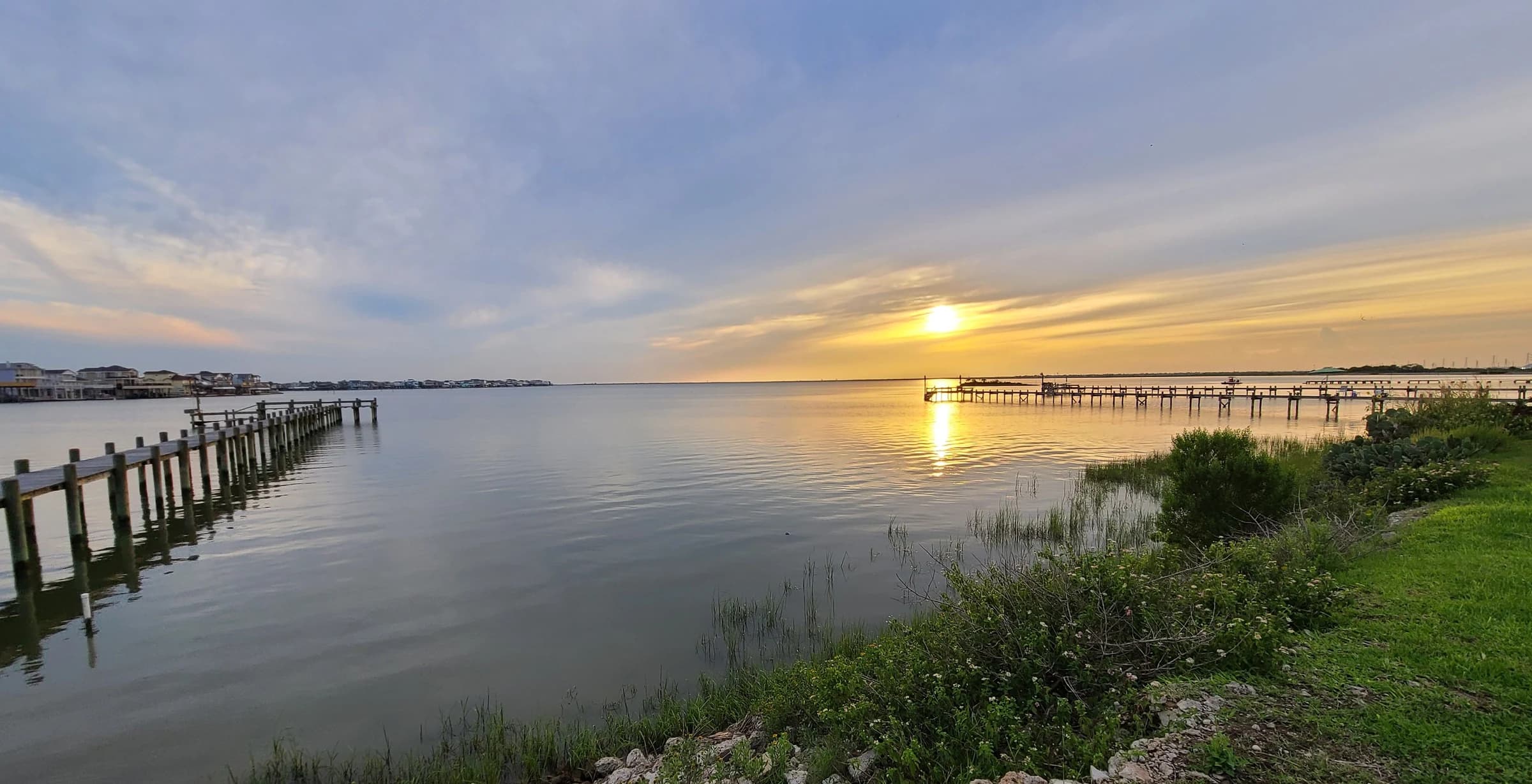 The setting sun reflects across the bay between long wooden fishing piers.